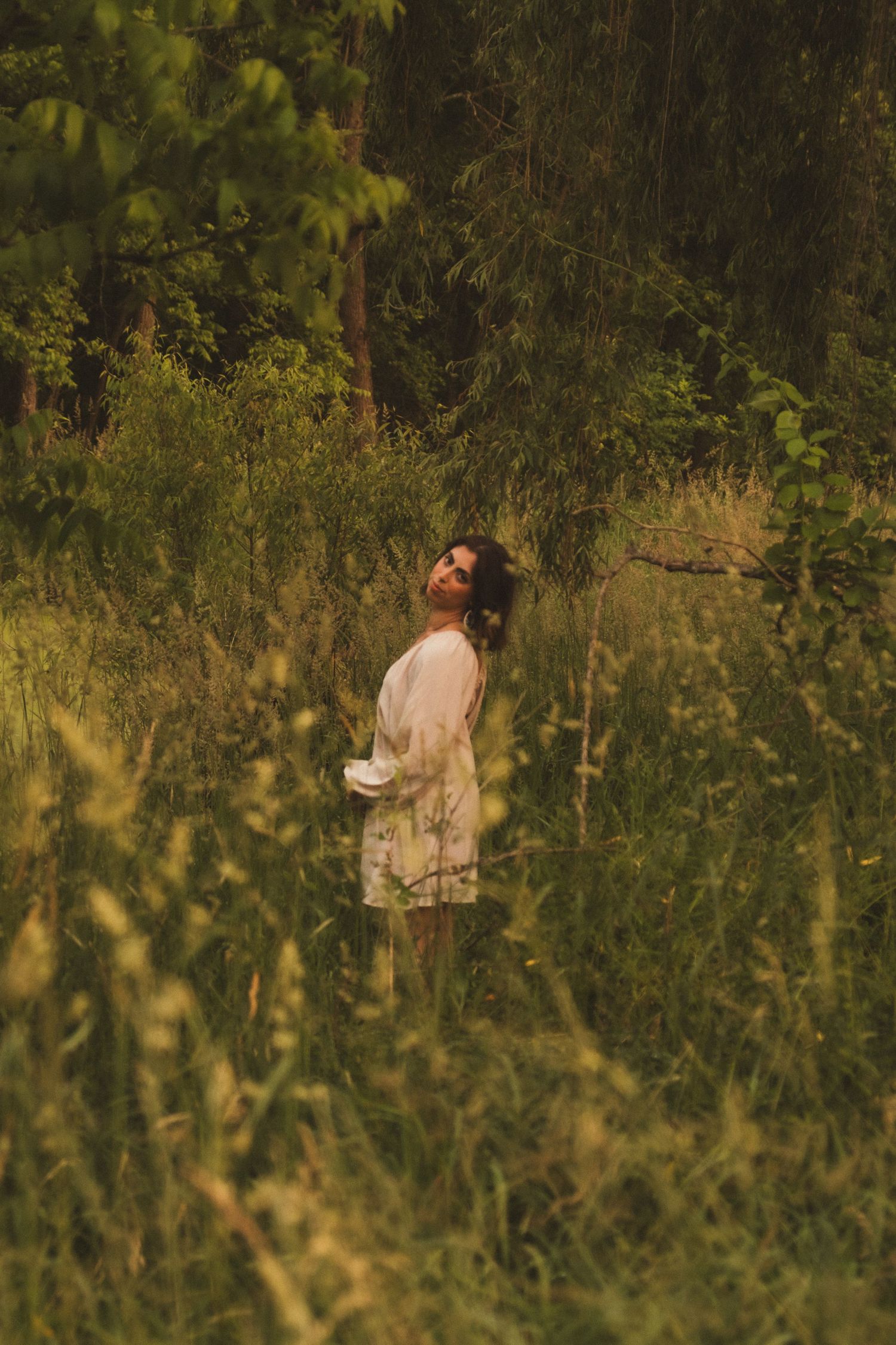 Person in light colored clothing walking through tall grass and wildflowers in golden evening light.