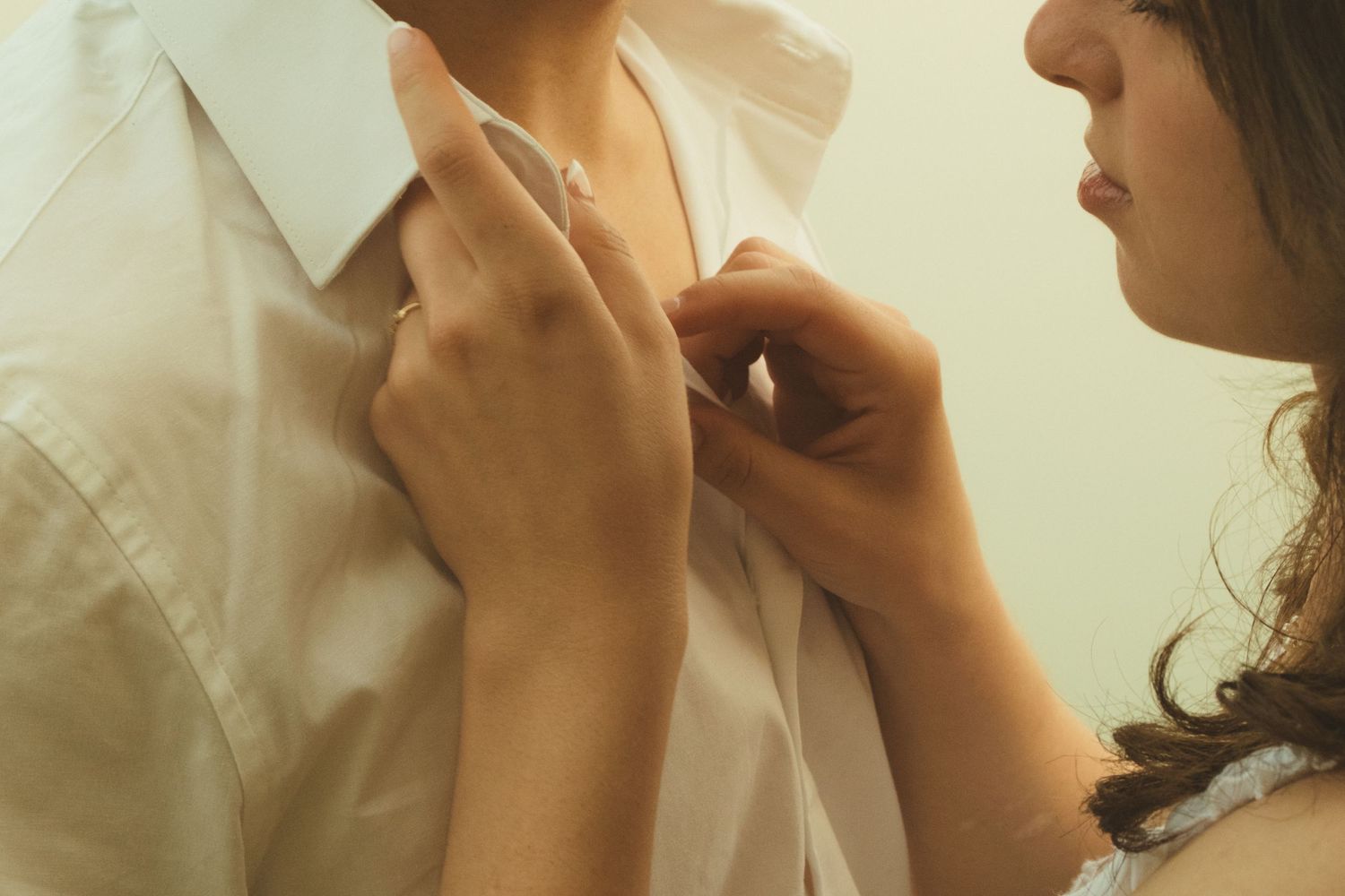 Woman helping a man button up his white dress shirt, close-up of hands adjusting collar.