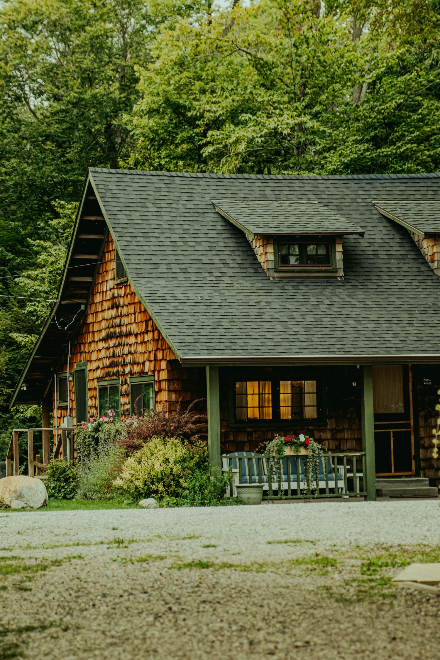 Rustic cedar shake cabin nestled among lush green trees with a covered porch and dormer window.