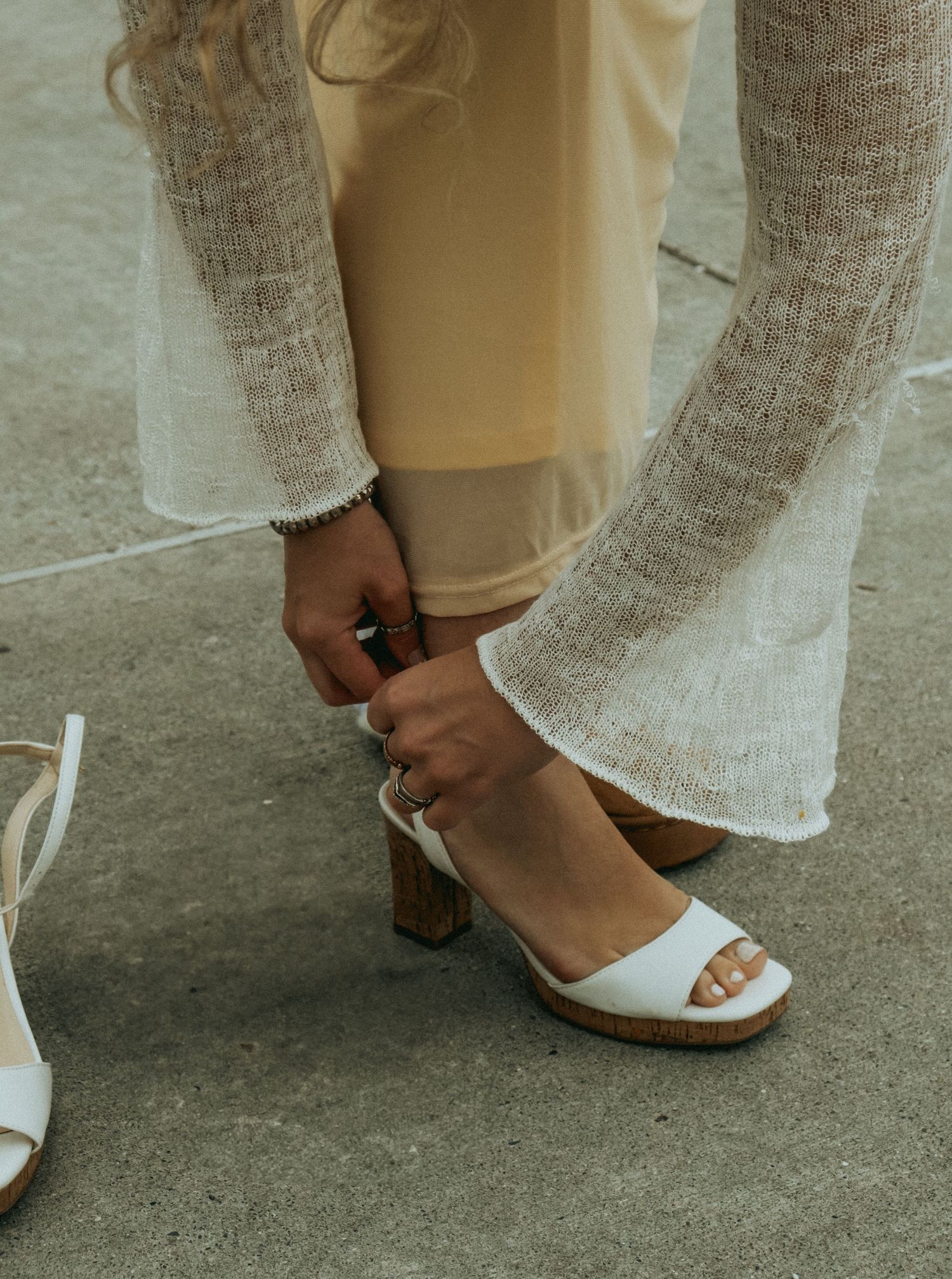 White wedding shoes being adjusted on concrete ground with lace dress fabric visible.