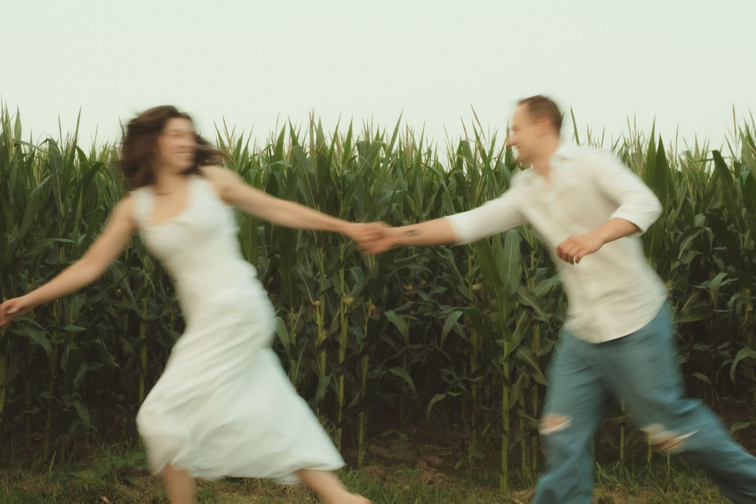 Couple dancing joyfully in front of a lush green cornfield, captured with motion blur effect.