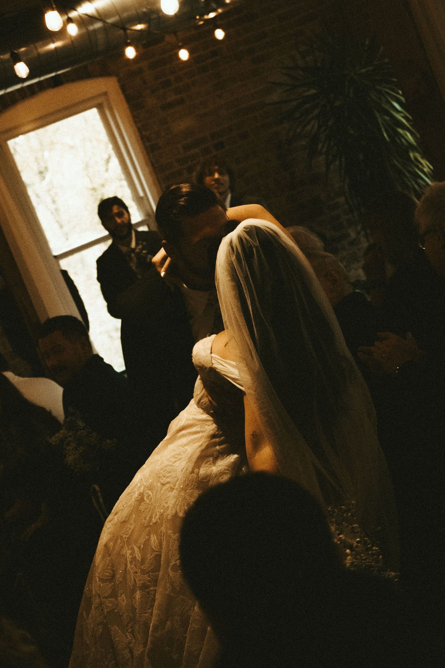 A silhouetted couple stands near a window in a dimly lit room with string lights creating a romantic ambiance.