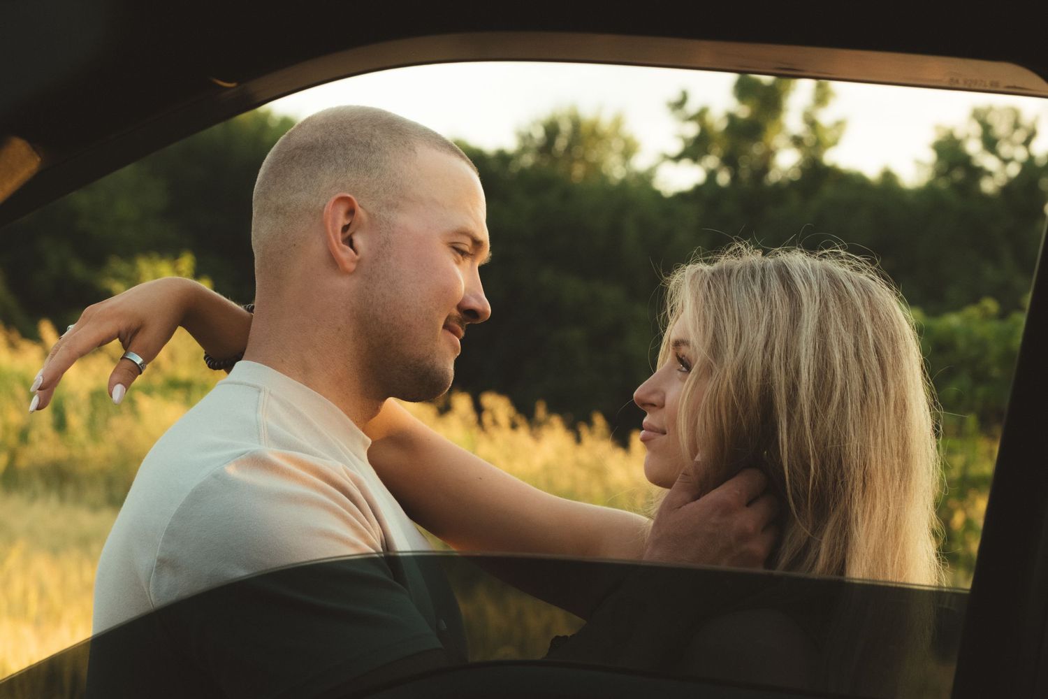 Romantic couple sharing an intimate moment by a car window in a golden sunset field.