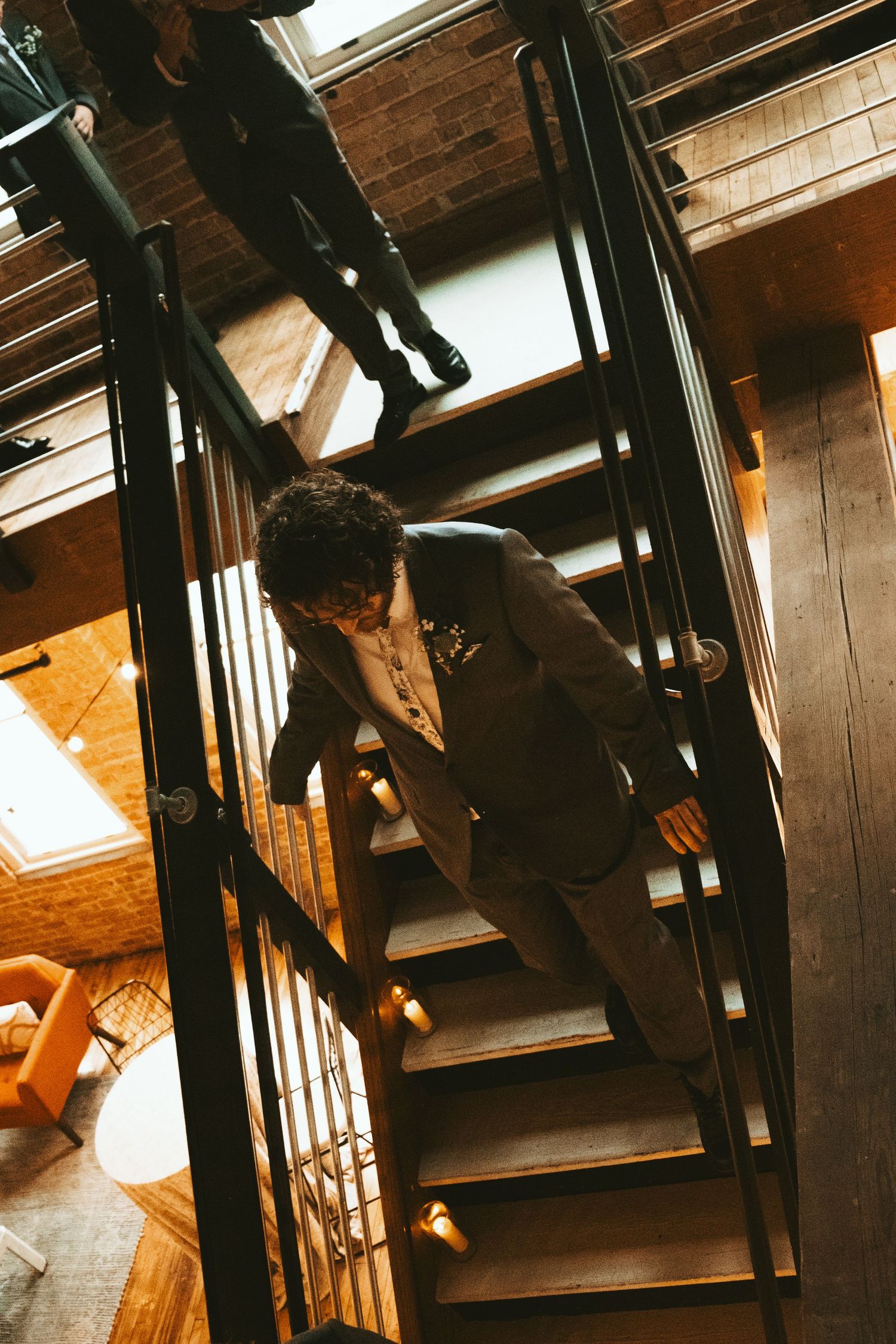 A person in a brown suit descends a dark industrial metal staircase inside a rustic wooden interior.