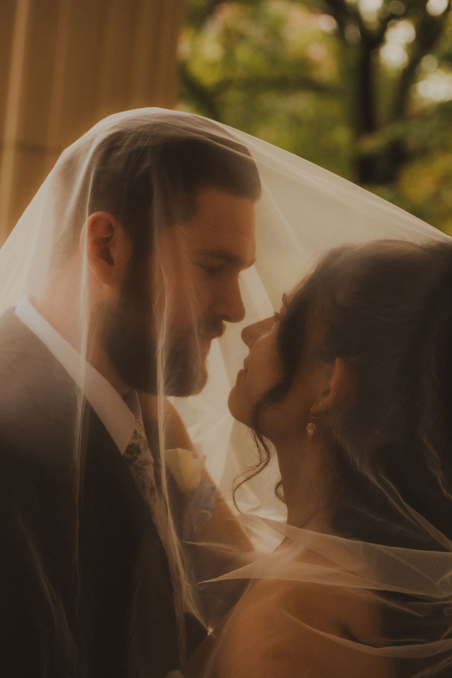 Romantic wedding couple shares an intimate moment under a flowing veil during golden hour.