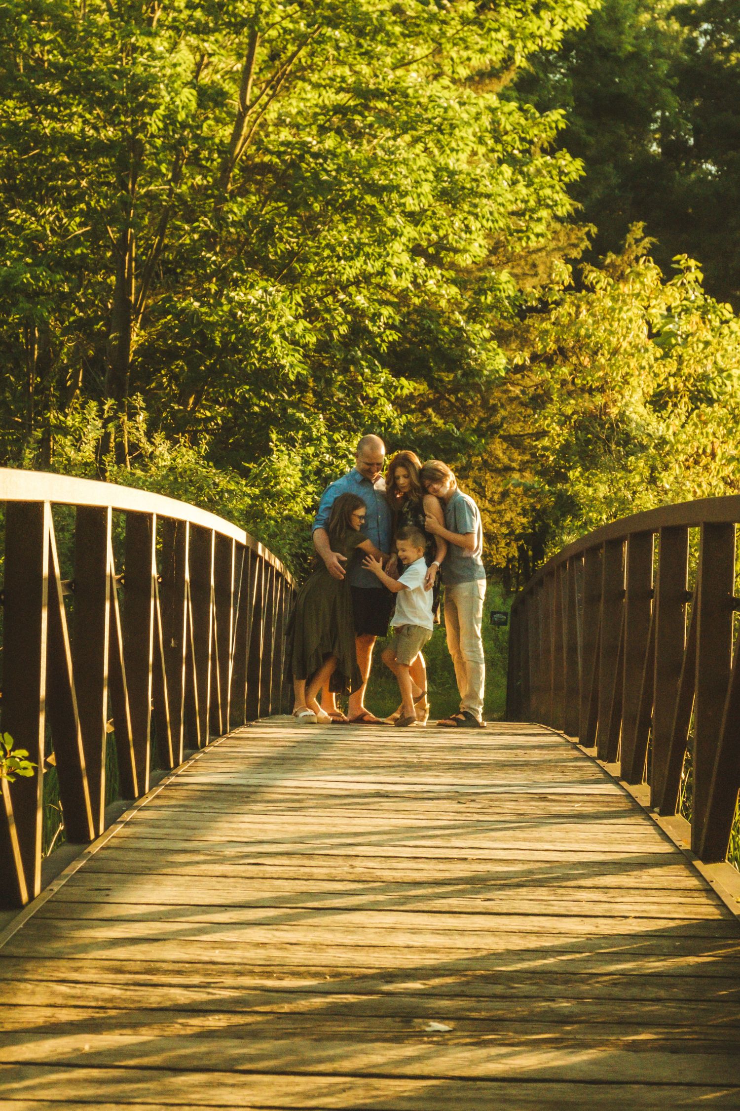 A sequence of photos showing people standing on a wooden bridge surrounded by golden sunlit trees in a park.