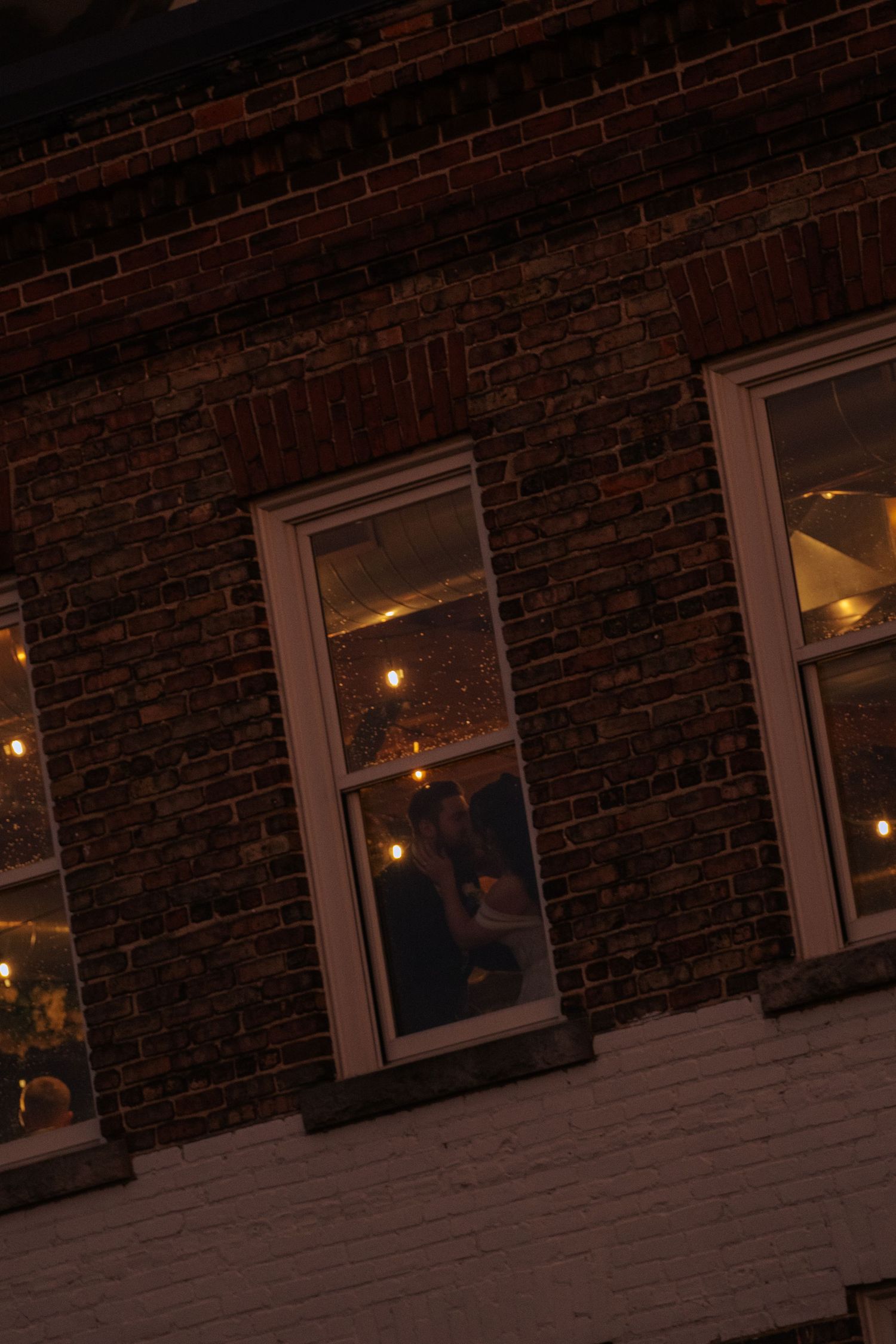 A row of illuminated windows along a dark brick wall creates a warm, moody nighttime atmosphere.