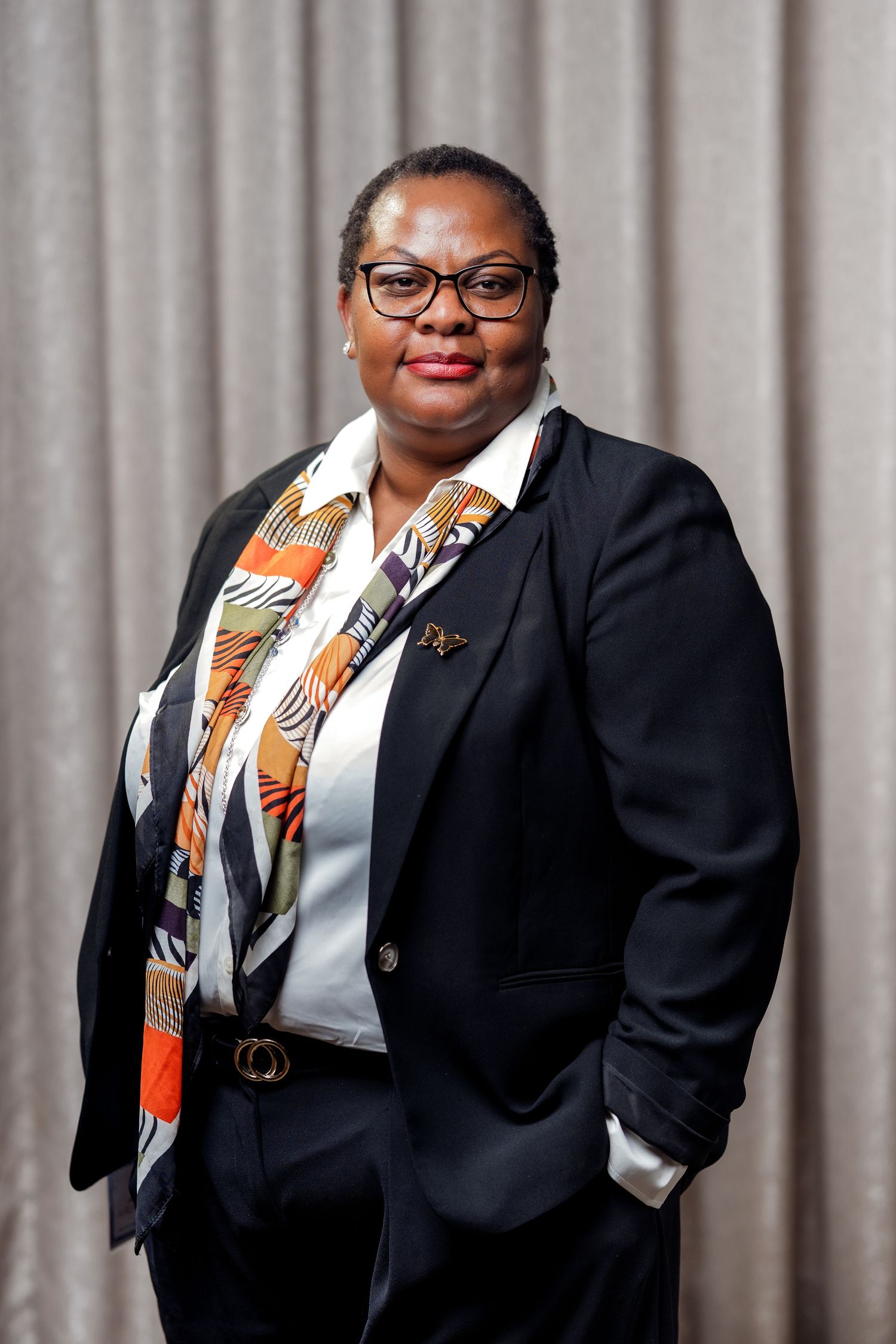 A portrait of a black woman in a black suit with her hands in her pockets