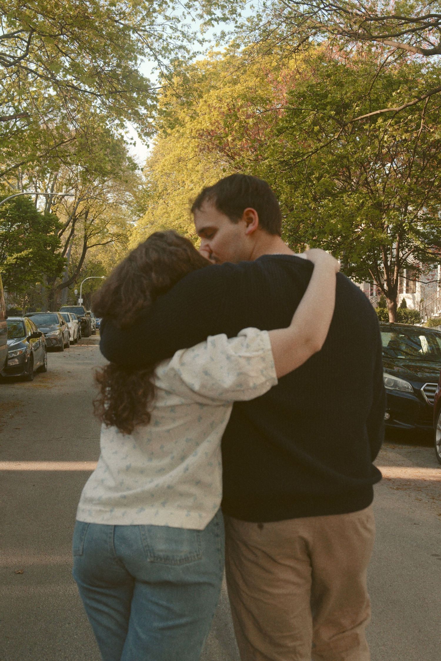 Two people embracing on a tree-lined residential street at dusk.