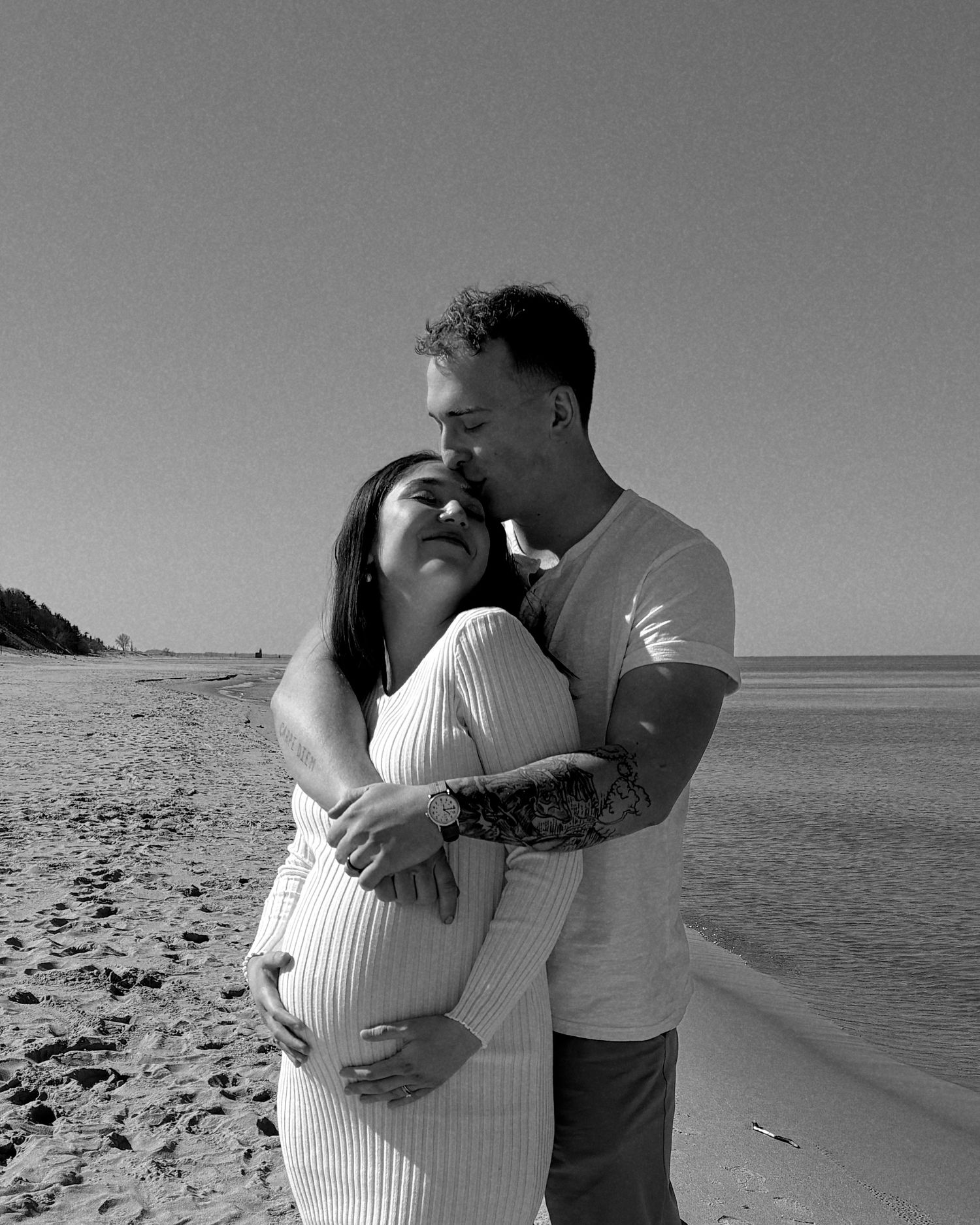 Tender black and white photo of a couple embracing on a beach shoreline.