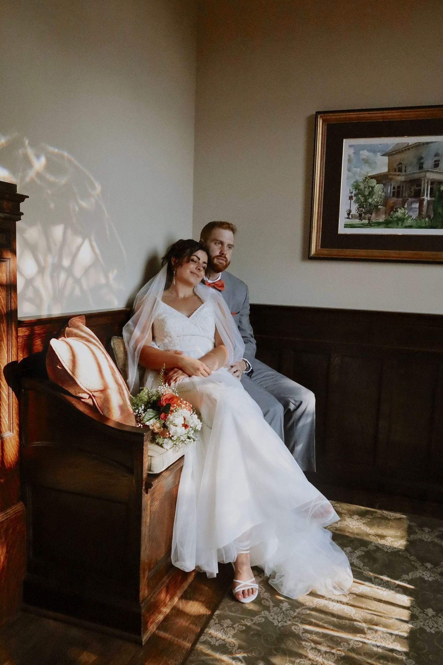 Wedding couple sits together in sunlit room with vintage wooden paneling.