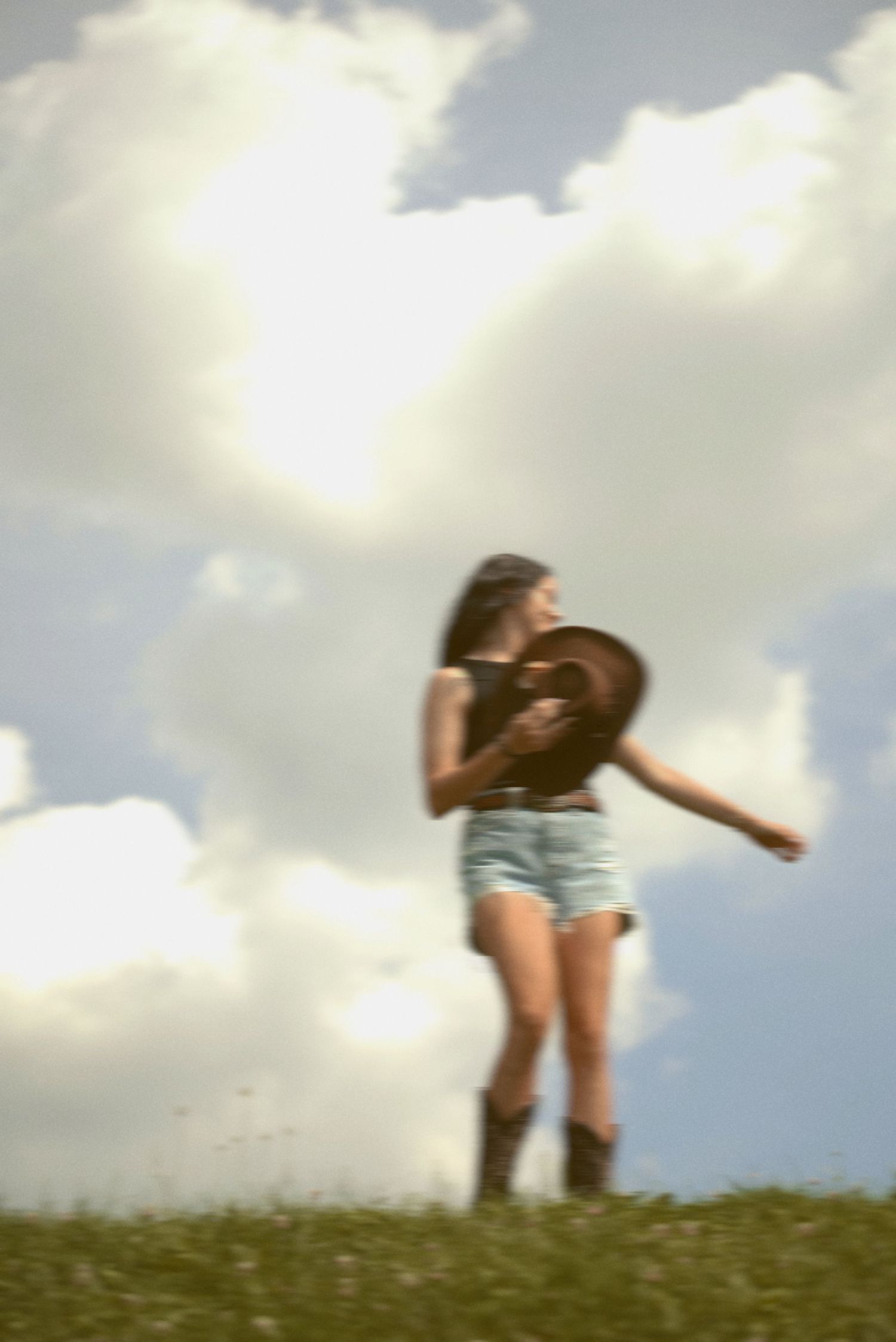 A person wearing denim shorts stands on a grassy hill against a cloudy sky in a dreamy, soft-focus photograph.