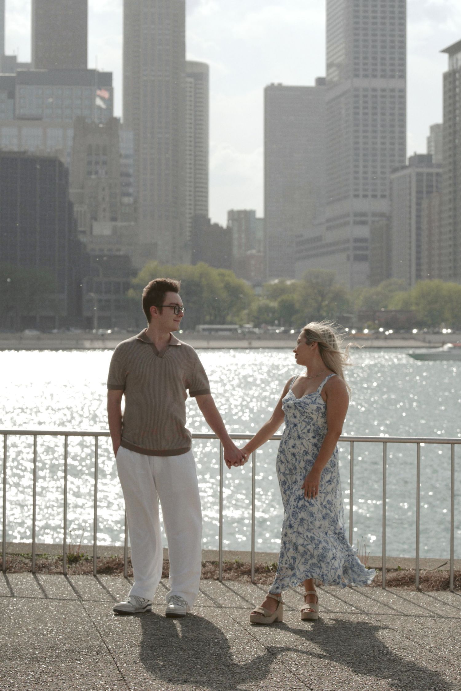 A couple holds hands while standing along Chicago's waterfront with the city skyline visible in the background.