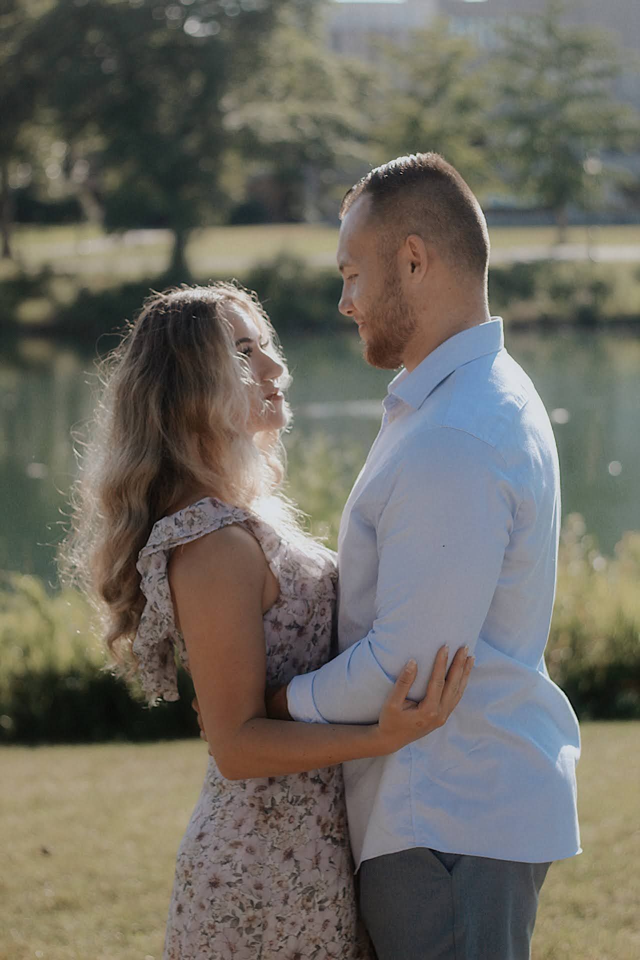 A couple shares intimate moments together outdoors by a lake in a romantic engagement photo series.