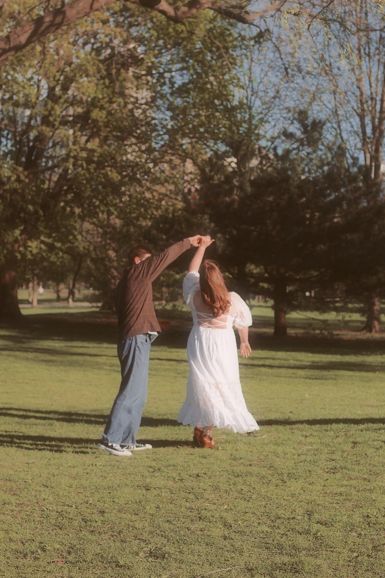 Two people on a grassy lawn performing ballet-like lift poses in a casual outdoor setting on a sunny day.