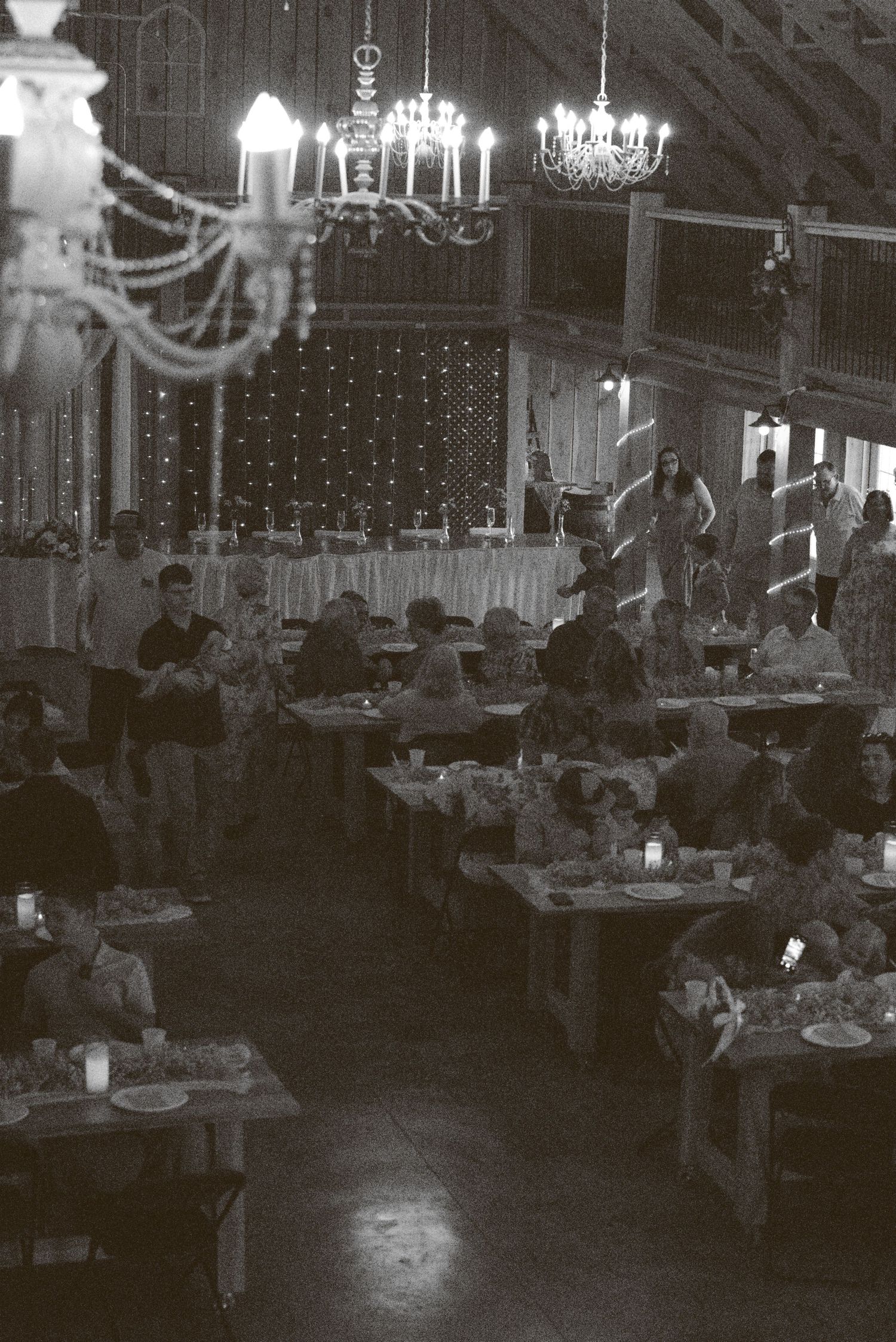 Black and white photo of an elegant banquet hall with crystal chandeliers and dining tables set for a formal event.