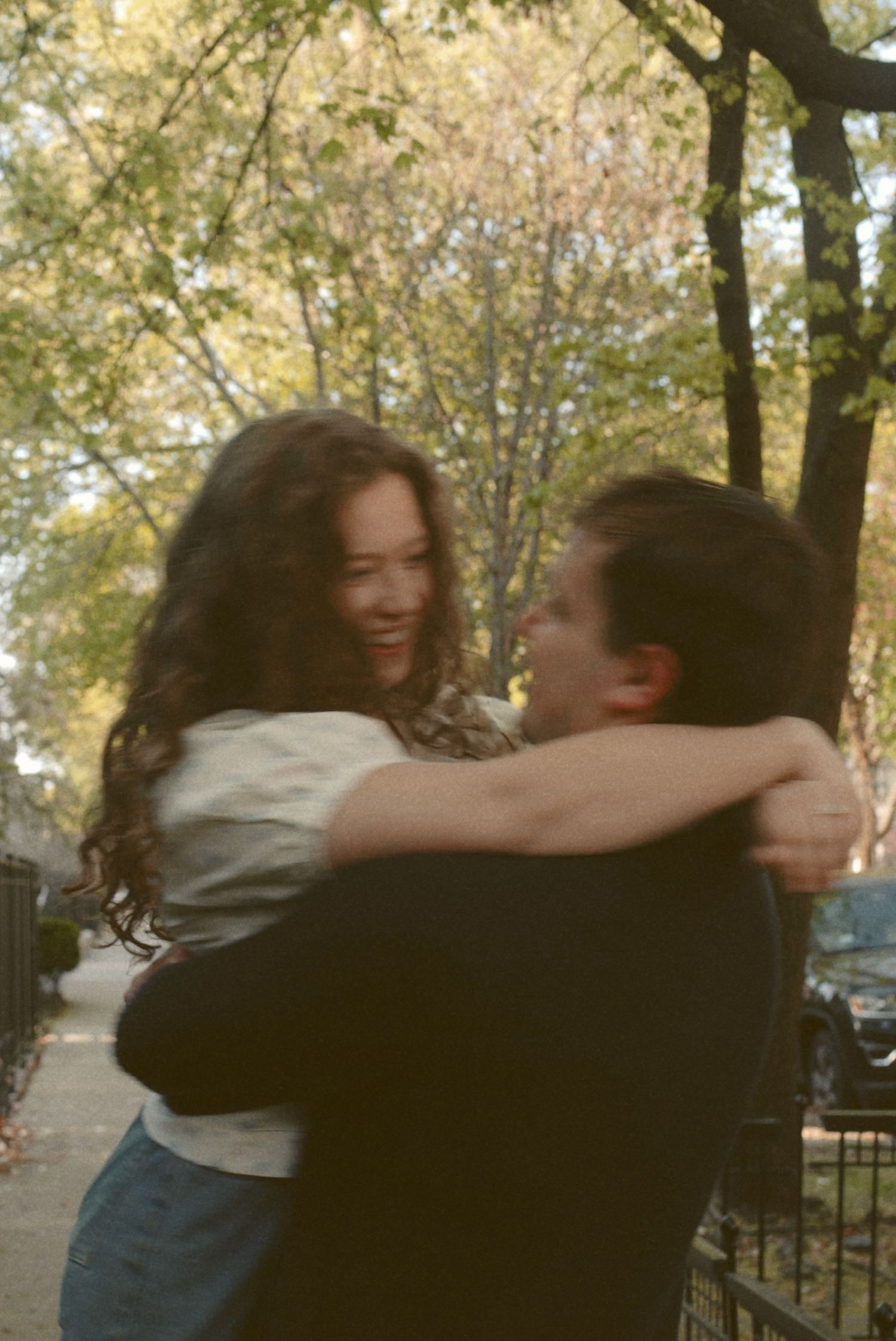 A joyful embrace captured in a candid moment on an autumn day with trees in the background.