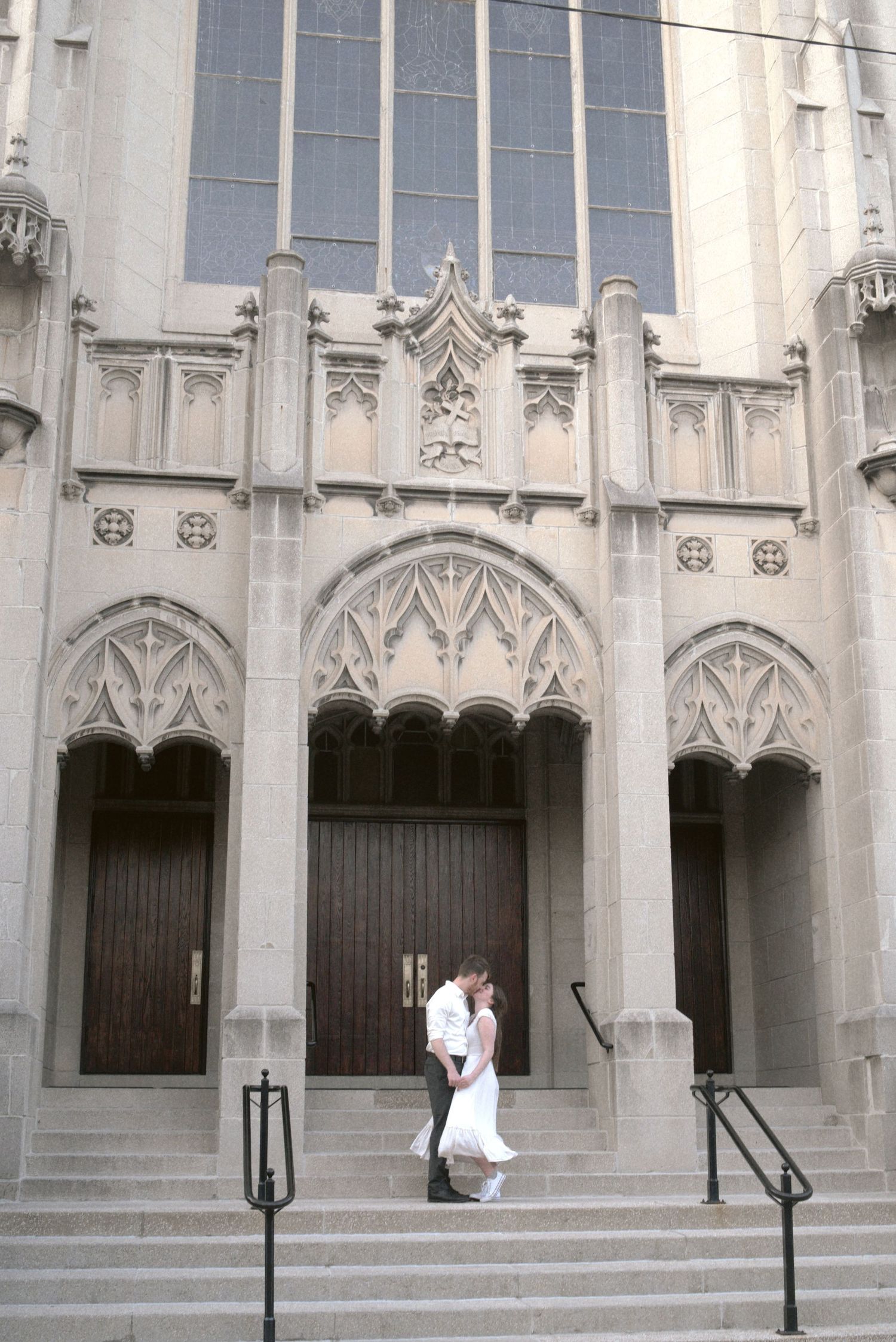 A couple shares a romantic moment on the steps of a Gothic-style church with ornate stone archways and decorative details.