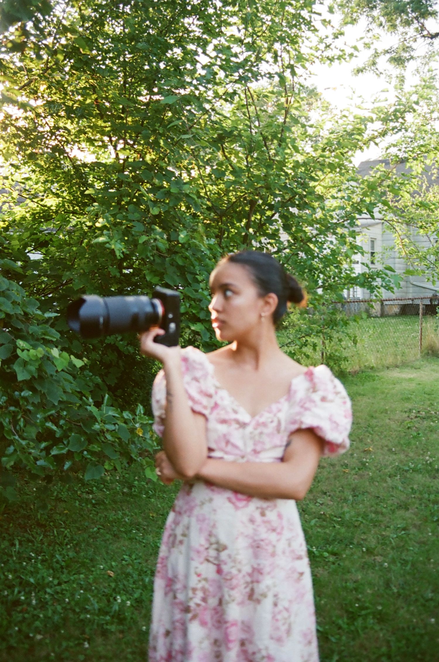 Someone wearing a pink floral dress uses a camera with a telephoto lens in a lush garden setting.