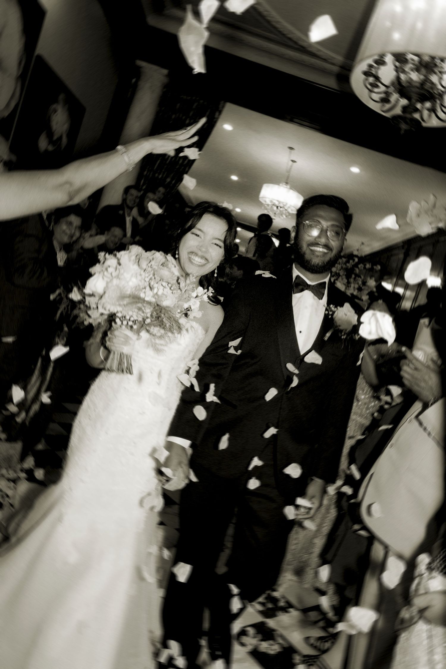 Bride and groom enjoy a celebratory moment as wedding guests throw white flower petals during their reception dance.