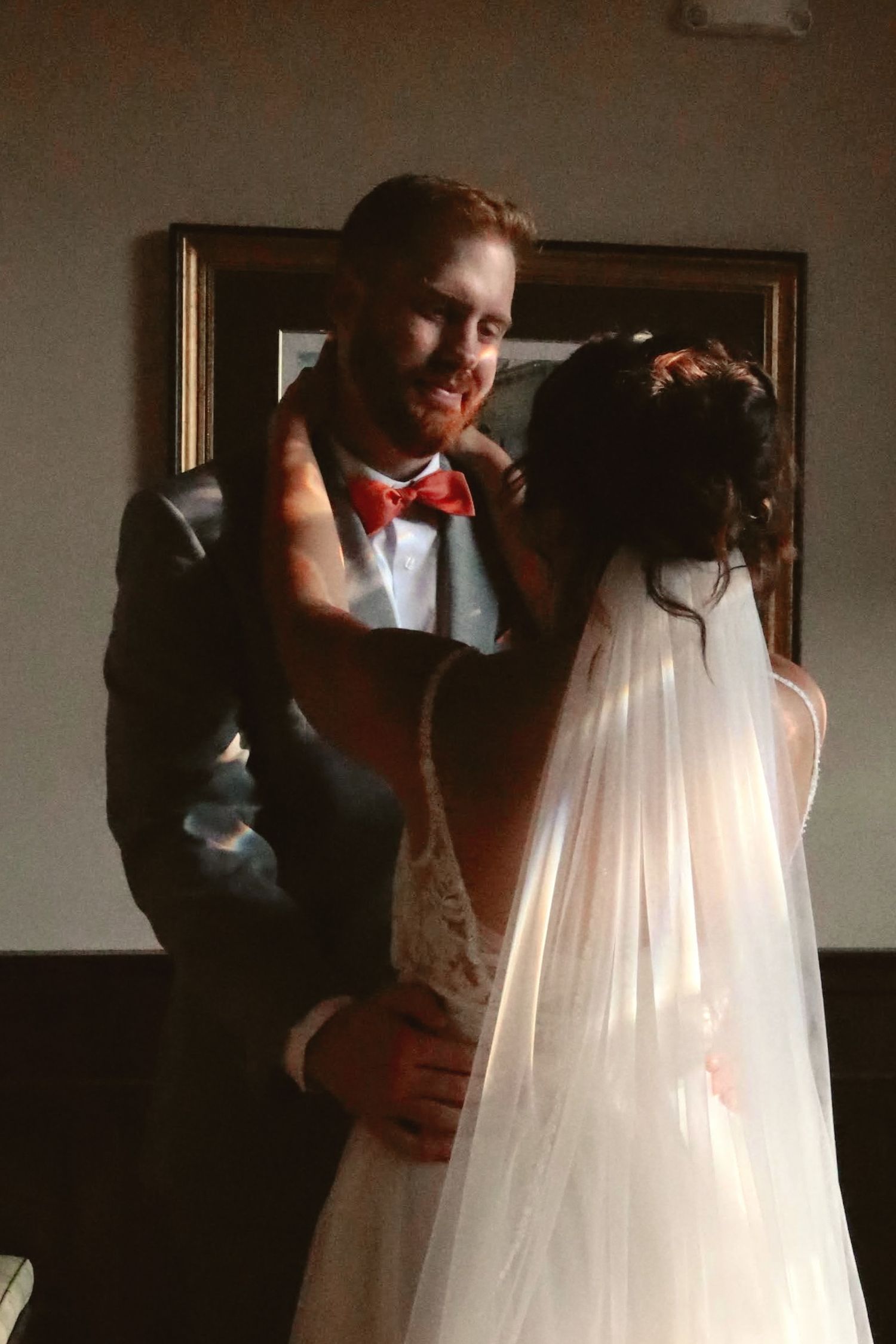 A wedding couple shares an intimate moment together, with the bride in white and groom wearing a red bow tie.