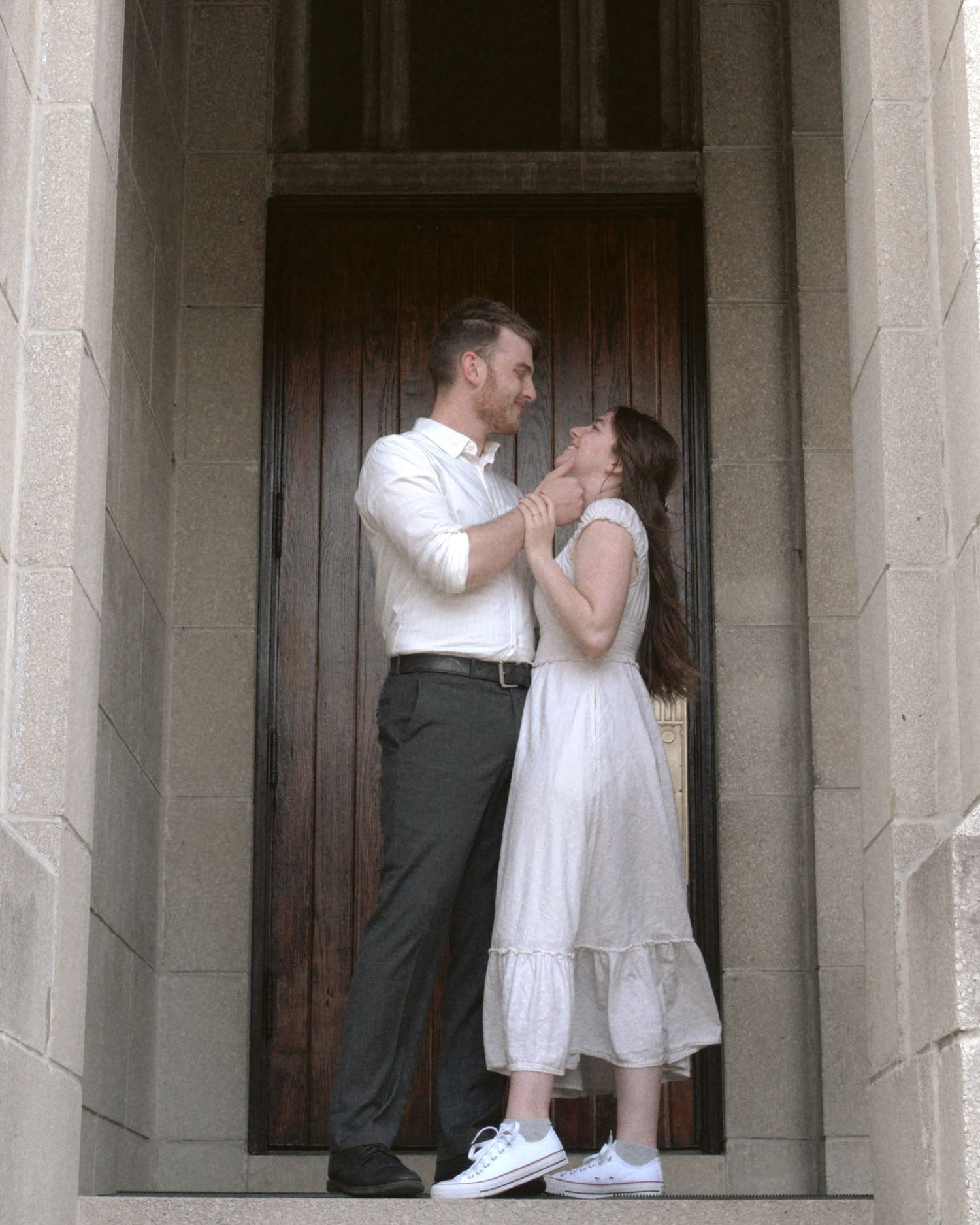 A couple shares a tender moment while standing in a doorway framed by stone columns.