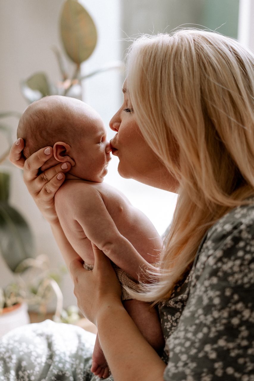 Mother lovingly and gently kissing her baby's nose at a newborn photoshoot in their Hampshire home.
