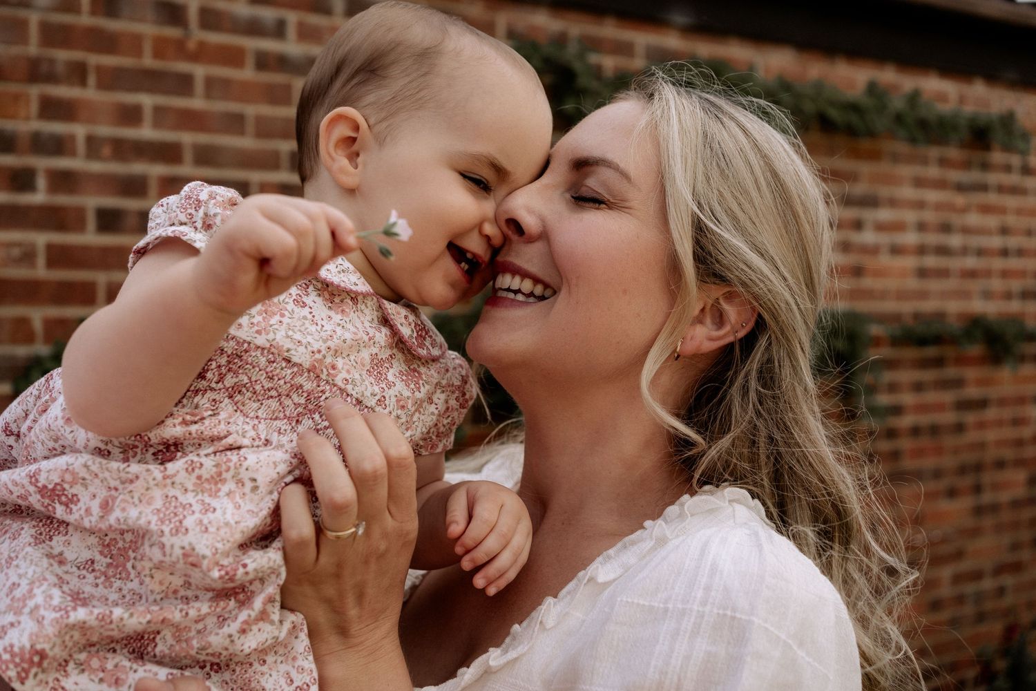 Mother holding her one year old baby girl, noses touching, both smiling with joy and beaming with love