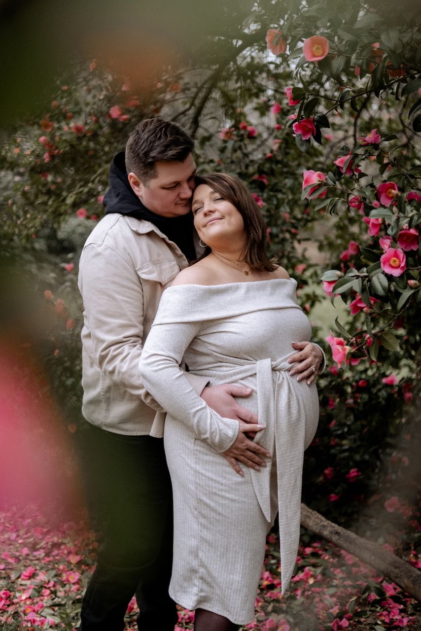 Male hugging his pregnant partner, both touching her bump and their heads lovingly touching at a maternity photoshoot in Surrey