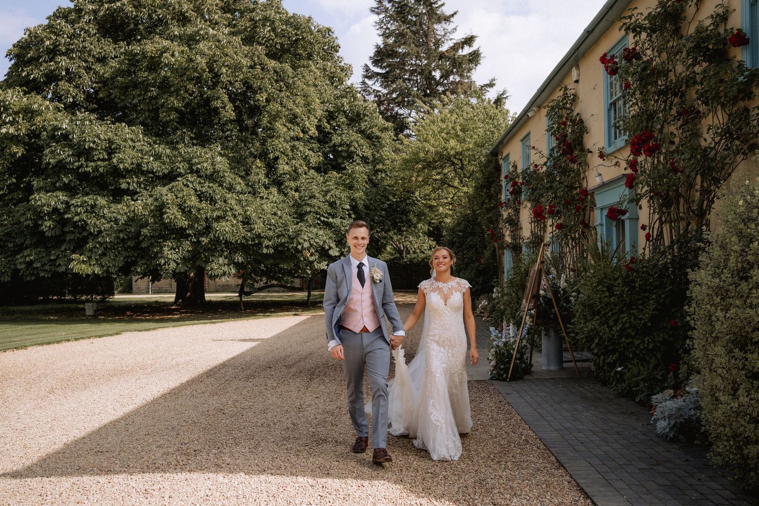 Bride and groom walking while holding hands and looking directly at the camera during a wedding at South Farm Royston, Hertfordshire