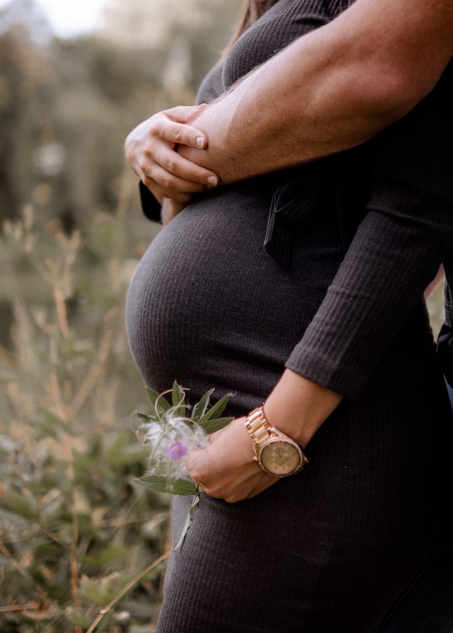 Close up shot of a pregnant belly showing male and female arms hugging