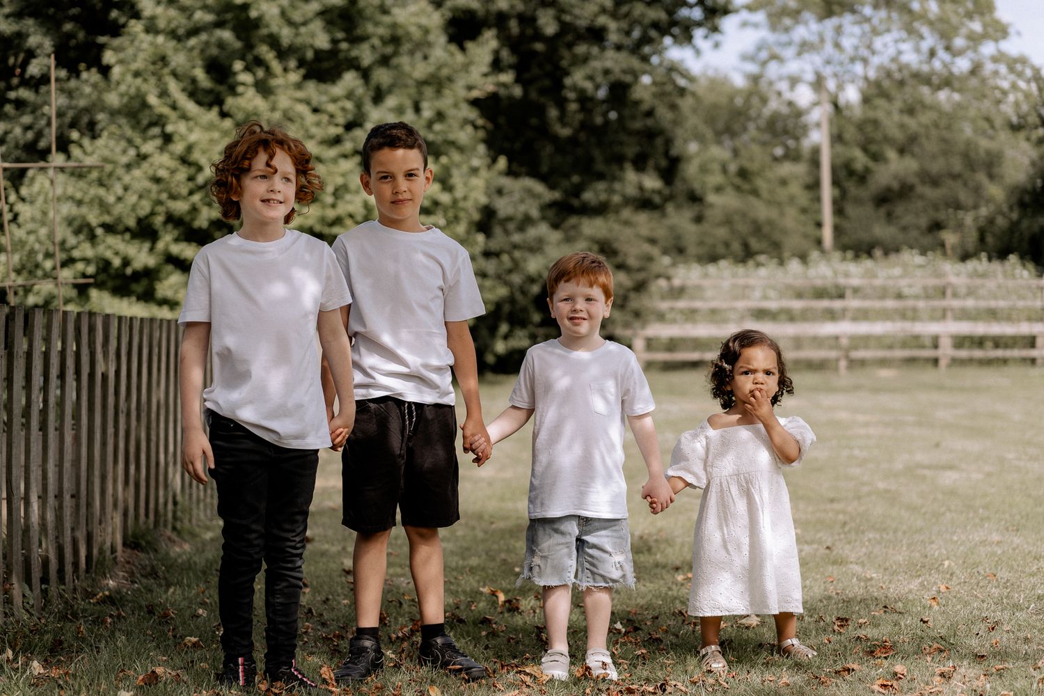 Four kids holding hands in their garden during a summer family photoshoot in Surrey, dressed in coordinating outfits and smiling