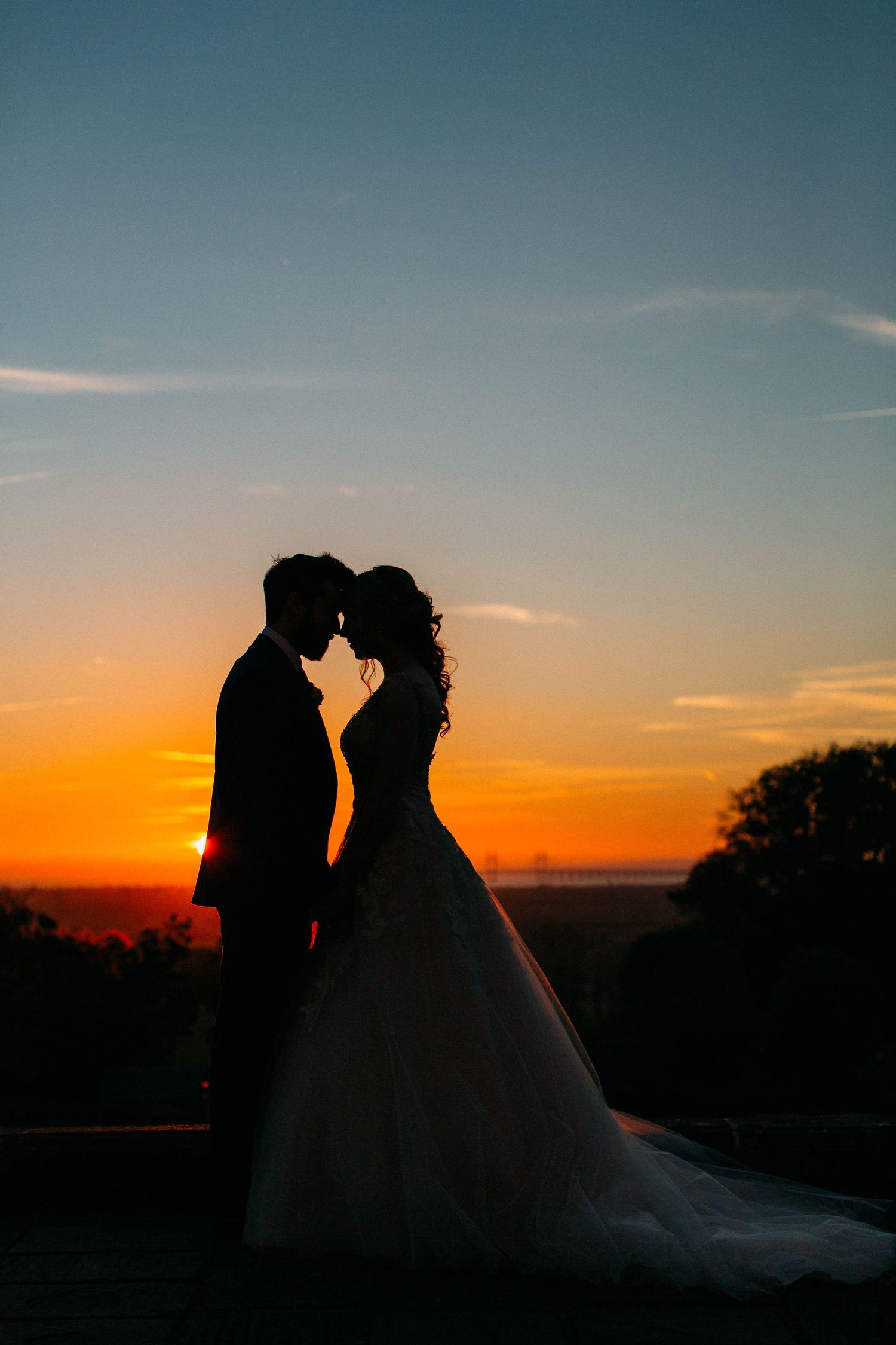 Silhouette of couple in wedding attire against vibrant orange sunset sky.