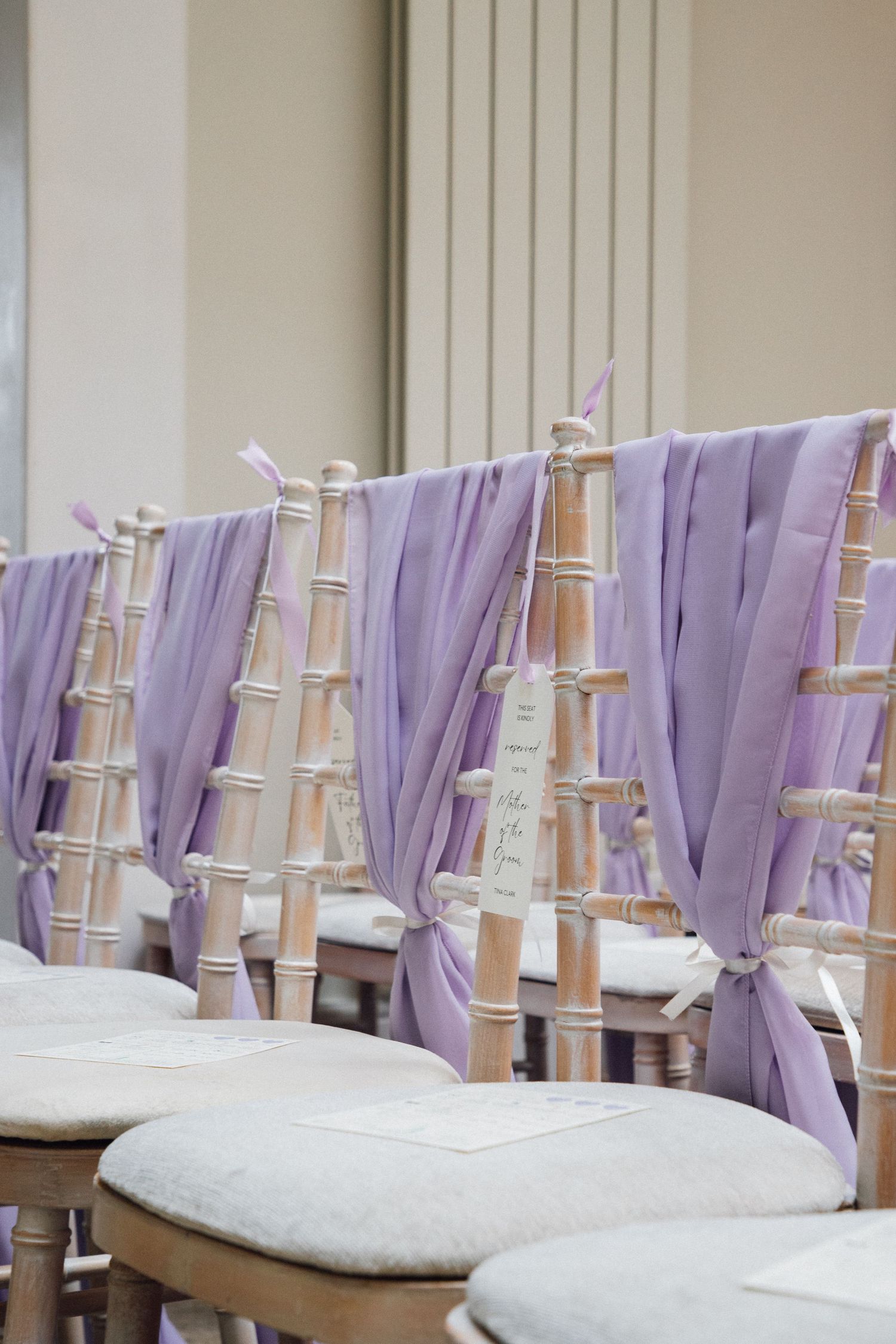 Elegant chiavari chairs with lavender fabric sashes and white cushions arranged for a formal event.