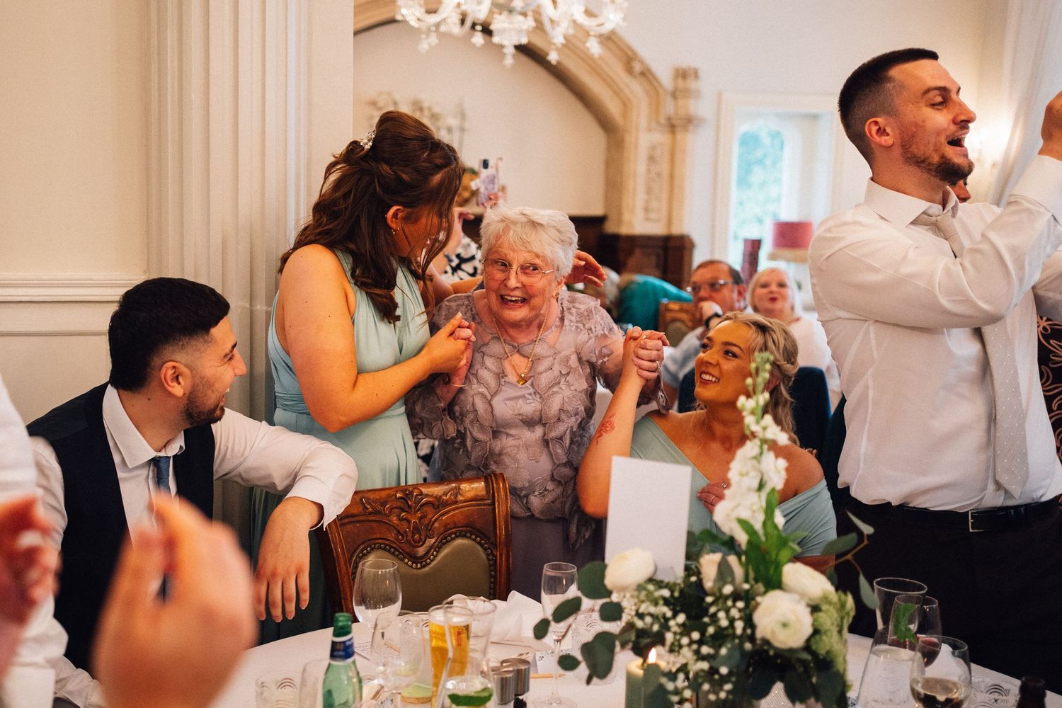 Guests share joyful moments around an elegant table decorated with floral centerpieces at a wedding reception.