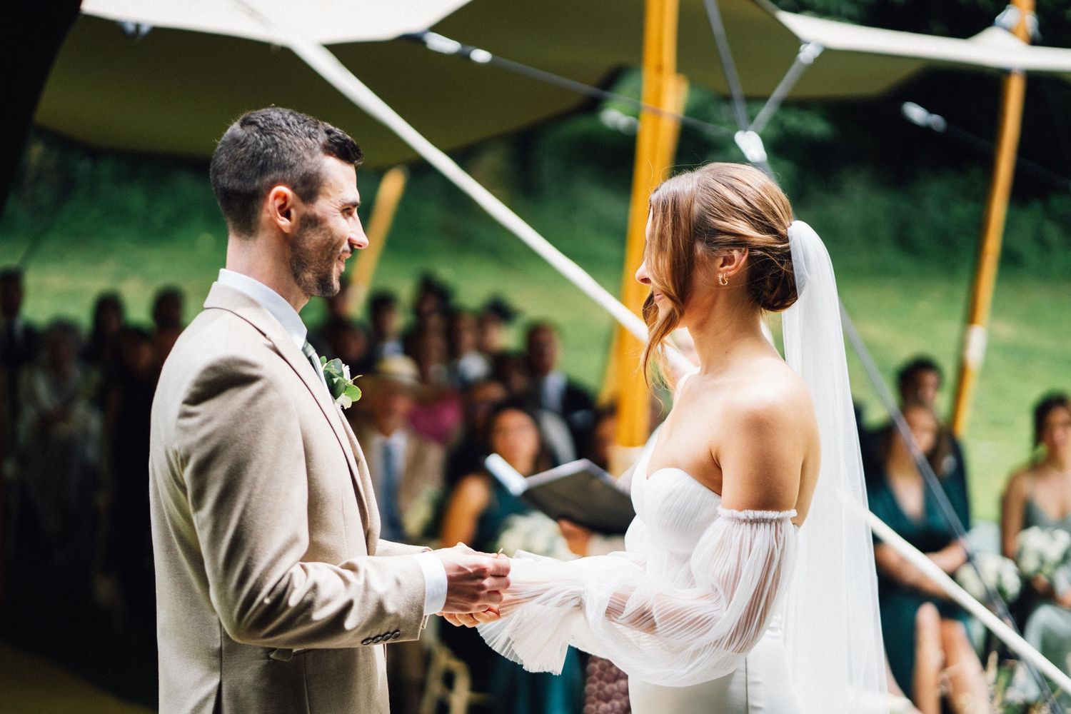A bride and groom hold hands during their wedding ceremony under a white tent canopy.