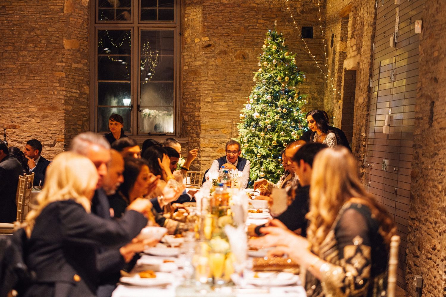 Wedding reception guests enjoying dinner in a warmly lit brick venue.