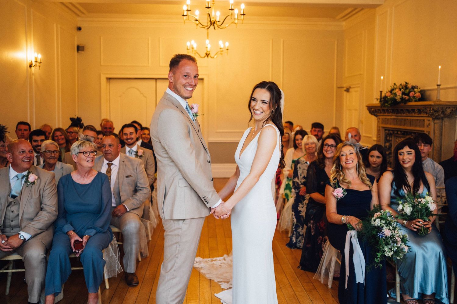 Elegant wedding reception in a grand ballroom with chandelier lighting and guests dancing.