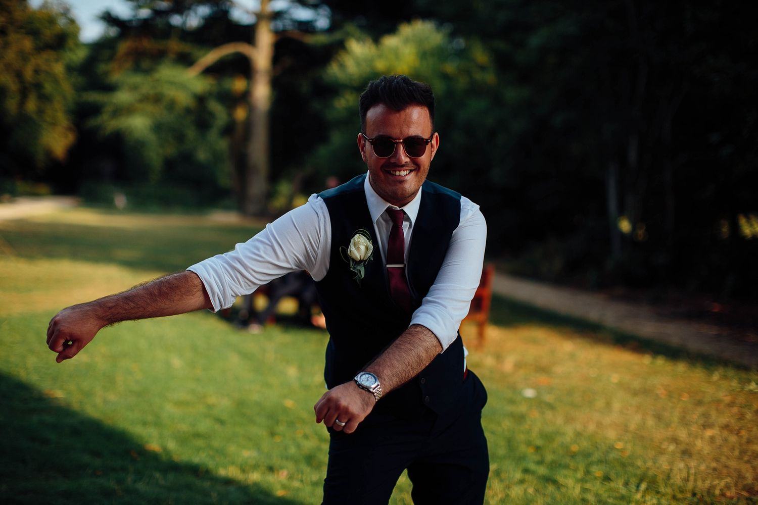 Person in formal attire striking a playful dance pose on a sunny lawn.