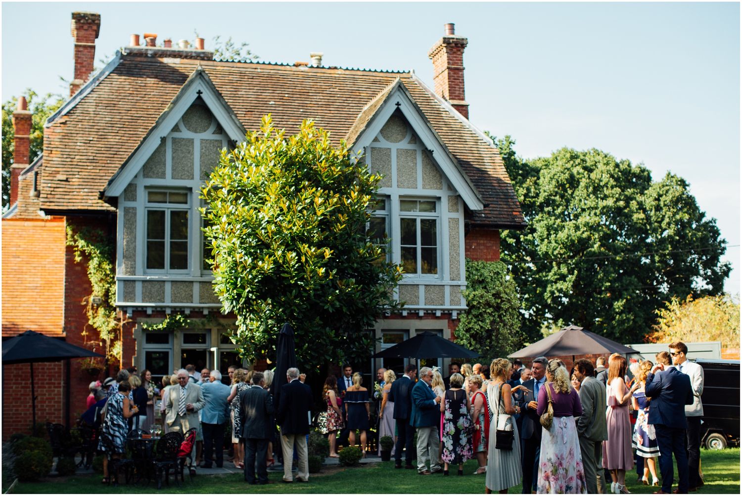 Traditional English cottage house serves as backdrop for outdoor wedding gathering.