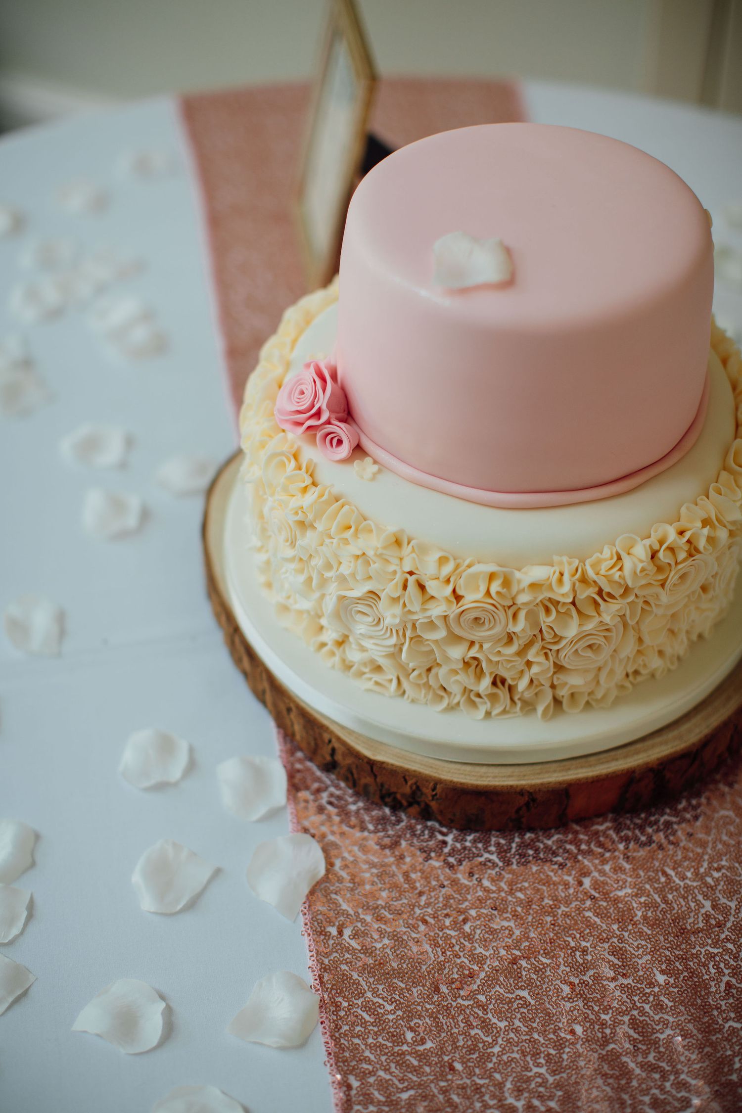 A delicate pink and cream wedding cake with ruffled frosting details and floral accents.