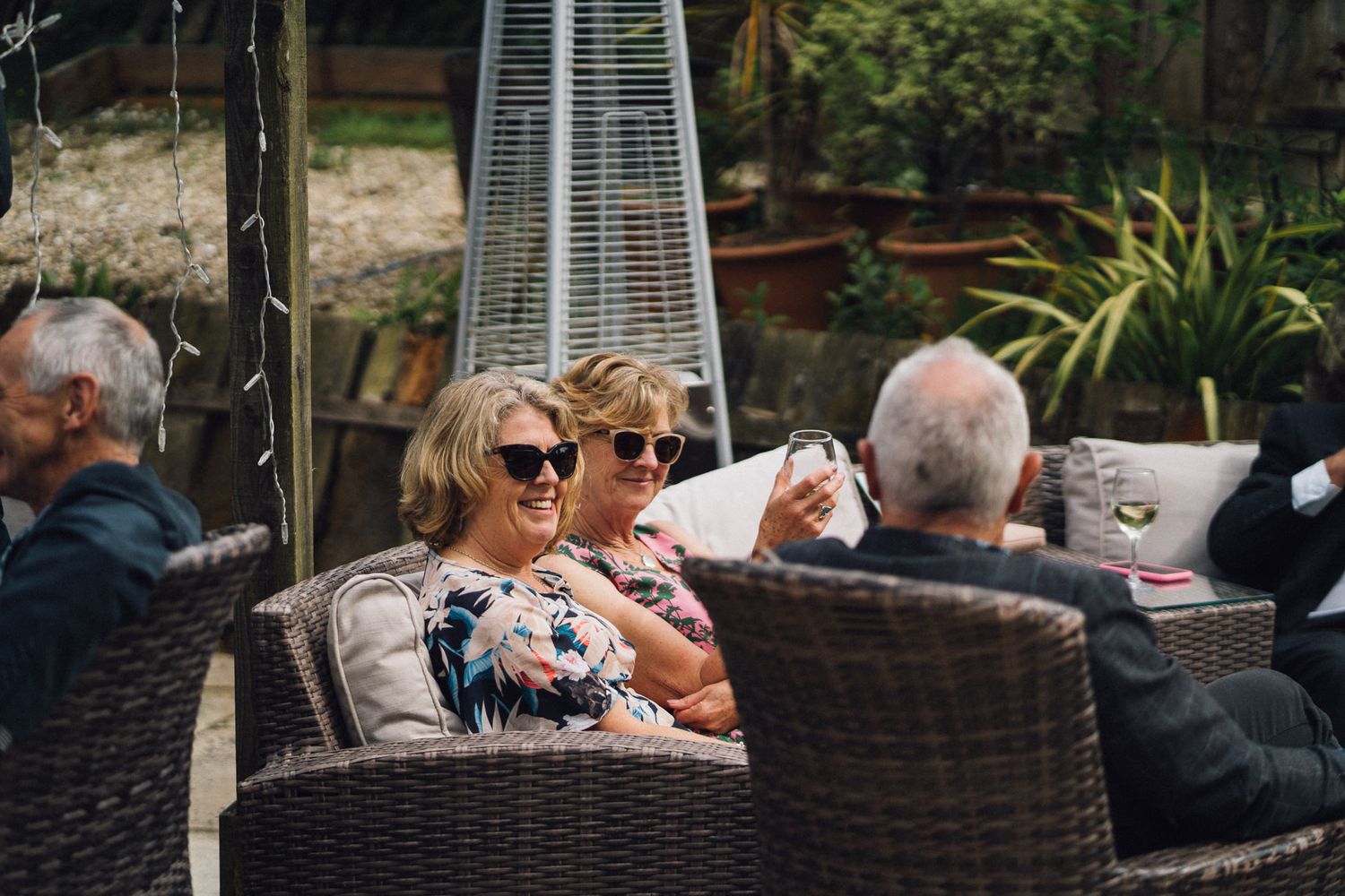 Guests relax in wicker patio furniture during outdoor wedding reception.