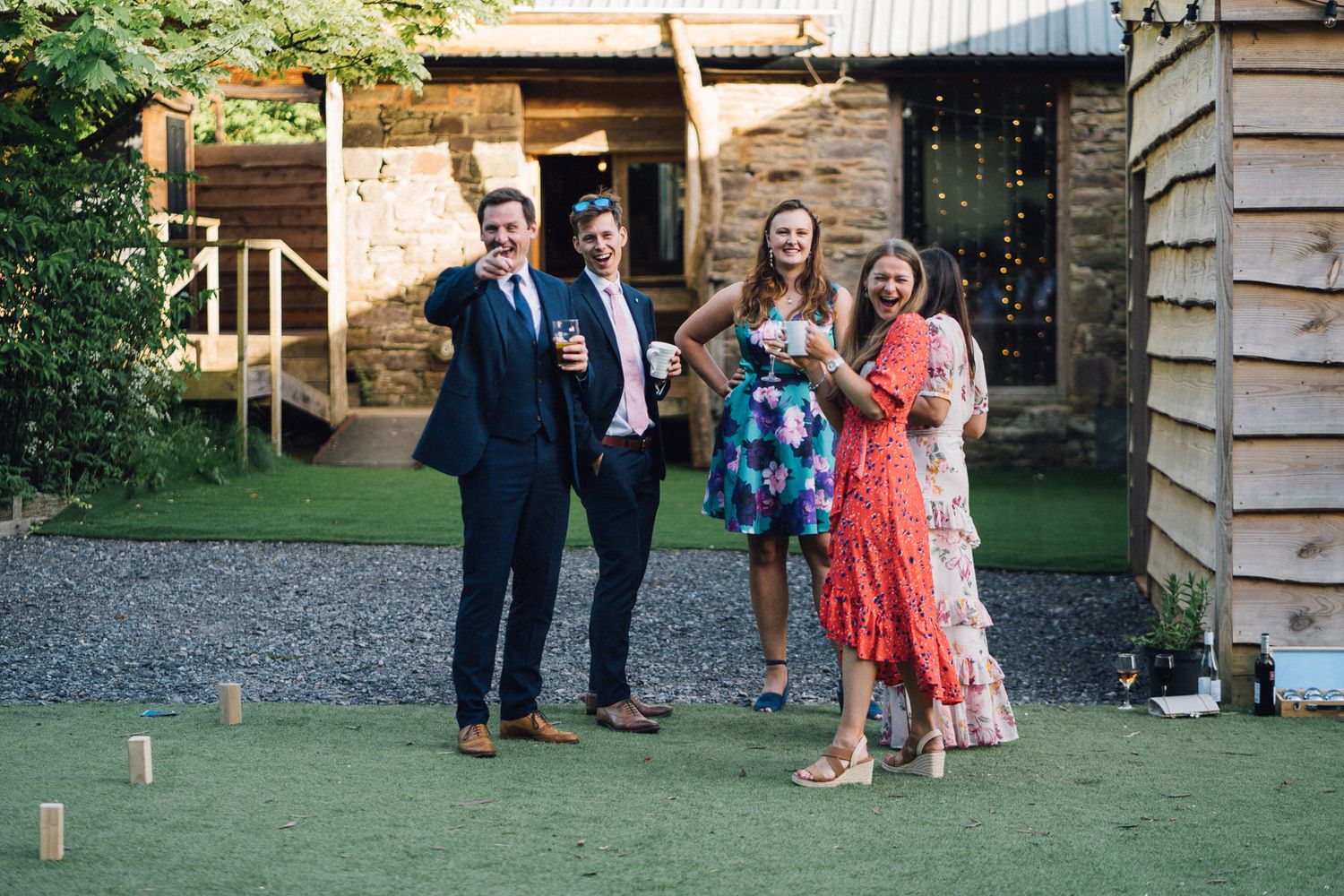 Wedding guests mingling on a lawn outside a rustic venue at dusk.