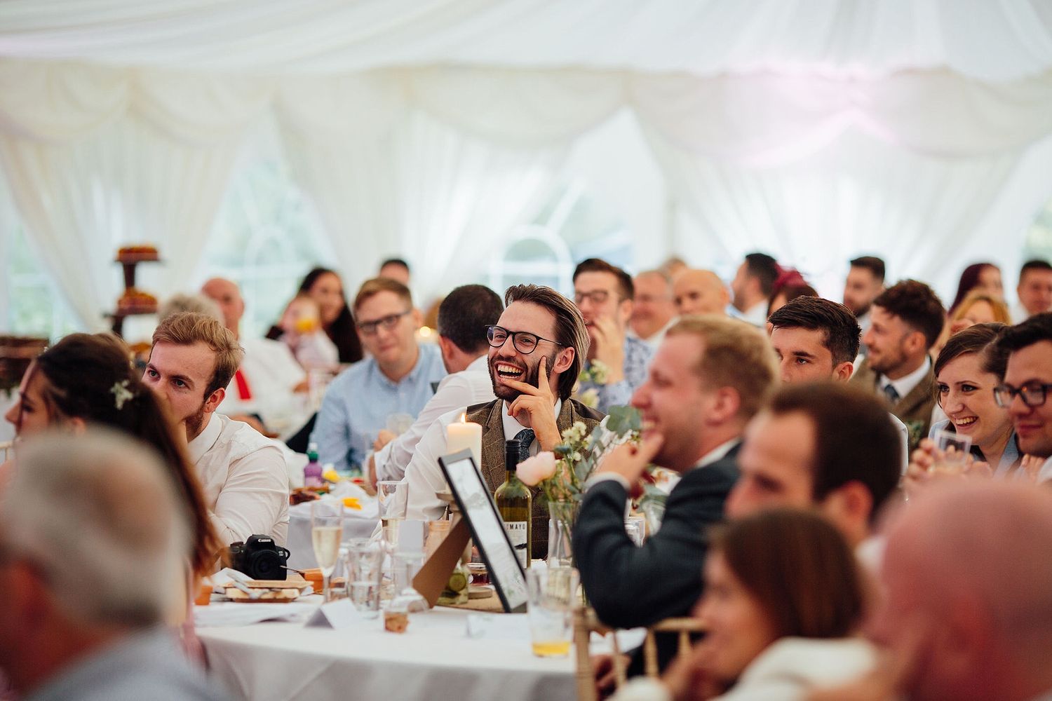 Large group of wedding guests seated and enjoying themselves at reception tables.