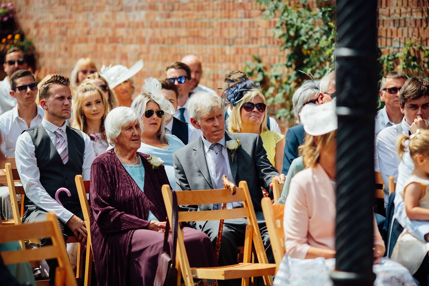 Wedding guests seated on wooden chairs during an outdoor garden ceremony.