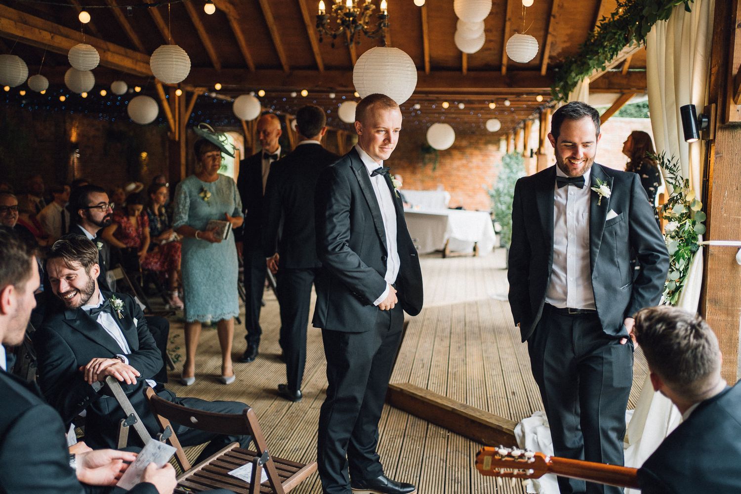 Wedding guests mingle and socialize in an elegant rustic barn venue decorated with hanging lights and chandeliers.