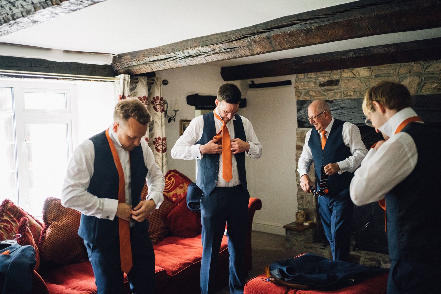 Group of groomsmen helping each other get dressed in formal wedding attire.