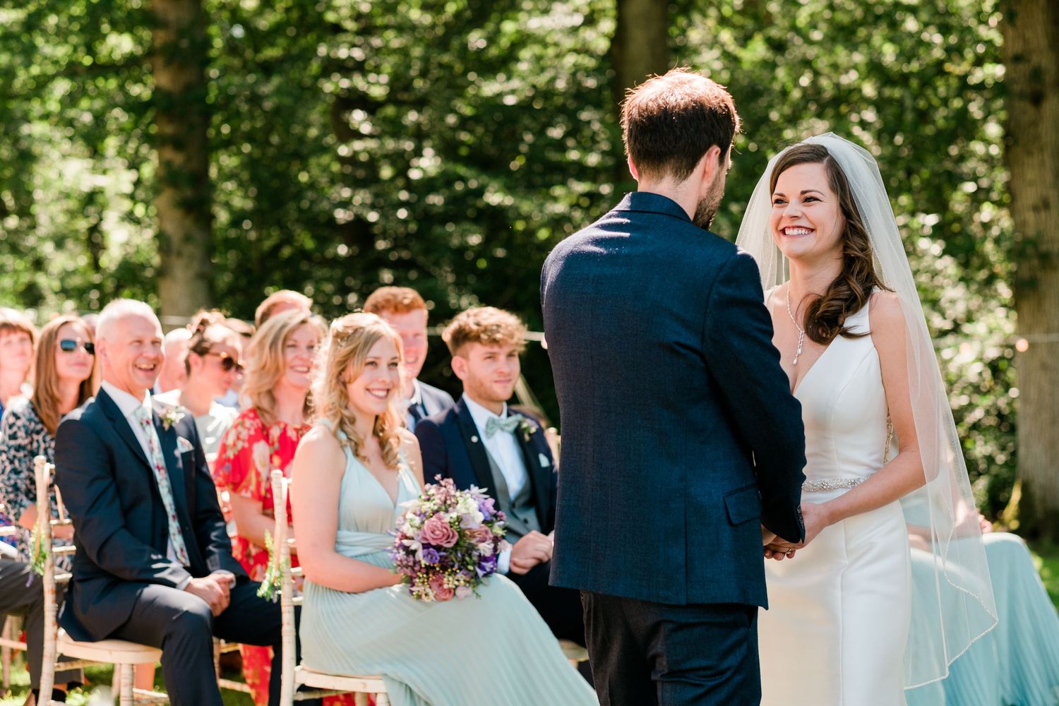 Intimate outdoor wedding ceremony with guests watching couple exchange vows.