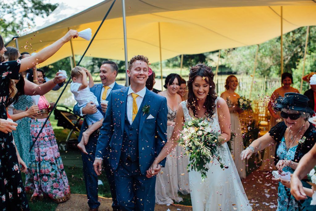 Wedding guests celebrate under a yellow tent canopy at an outdoor reception.