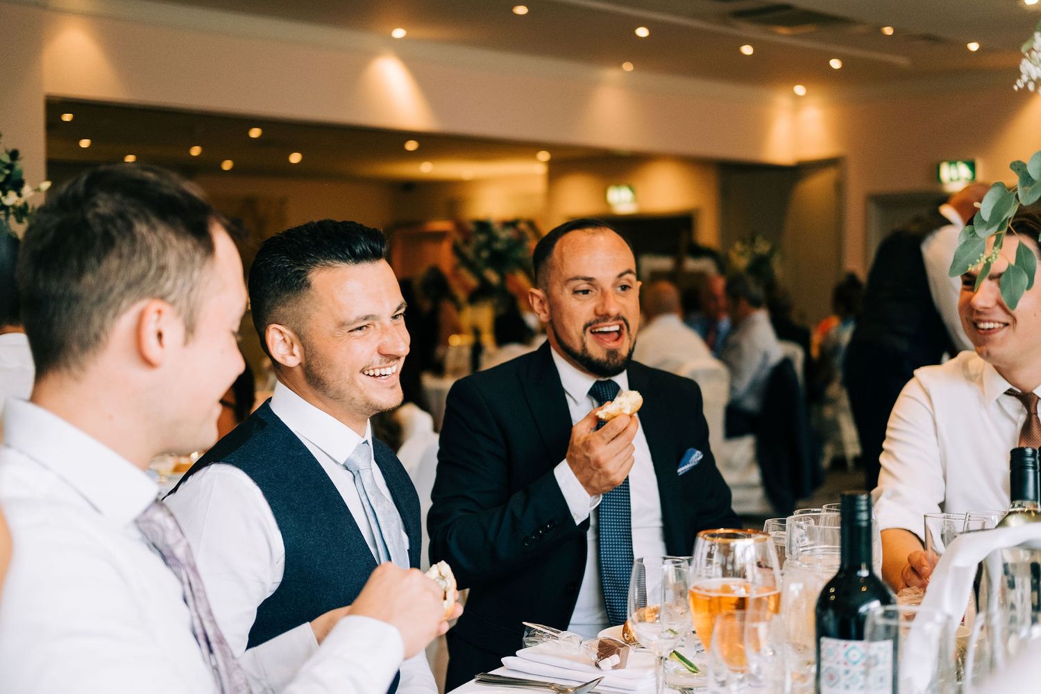 Wedding reception guests enjoying drinks and conversation at dining tables.